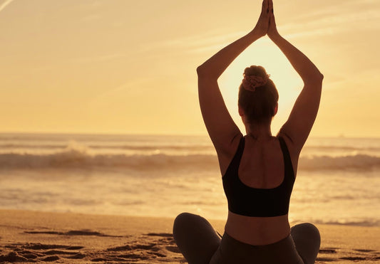 Vrouw mediteert op het strand tijdens zonsondergang