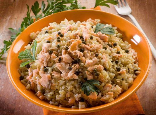 Romige zalmrisotto met groene peperkorrels en peterselie in een oranje kom